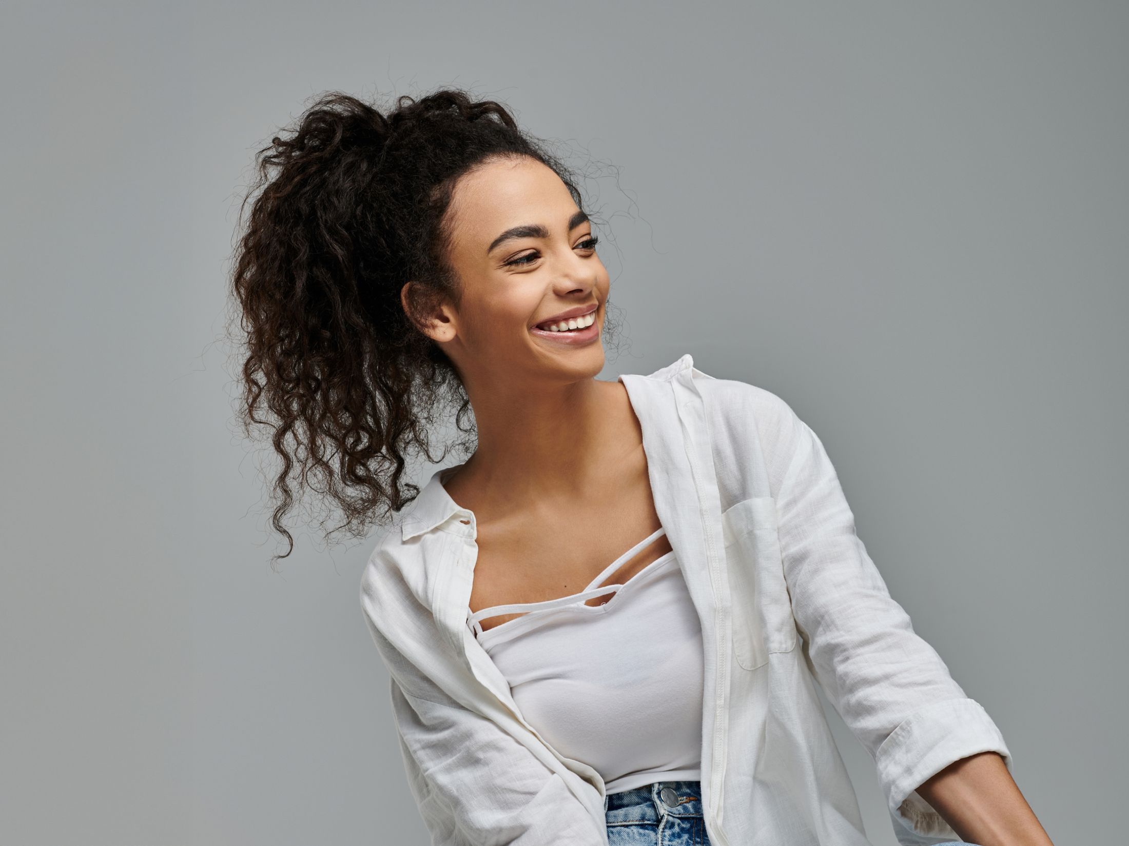 Smiling woman with curly hair in stylish outfit.