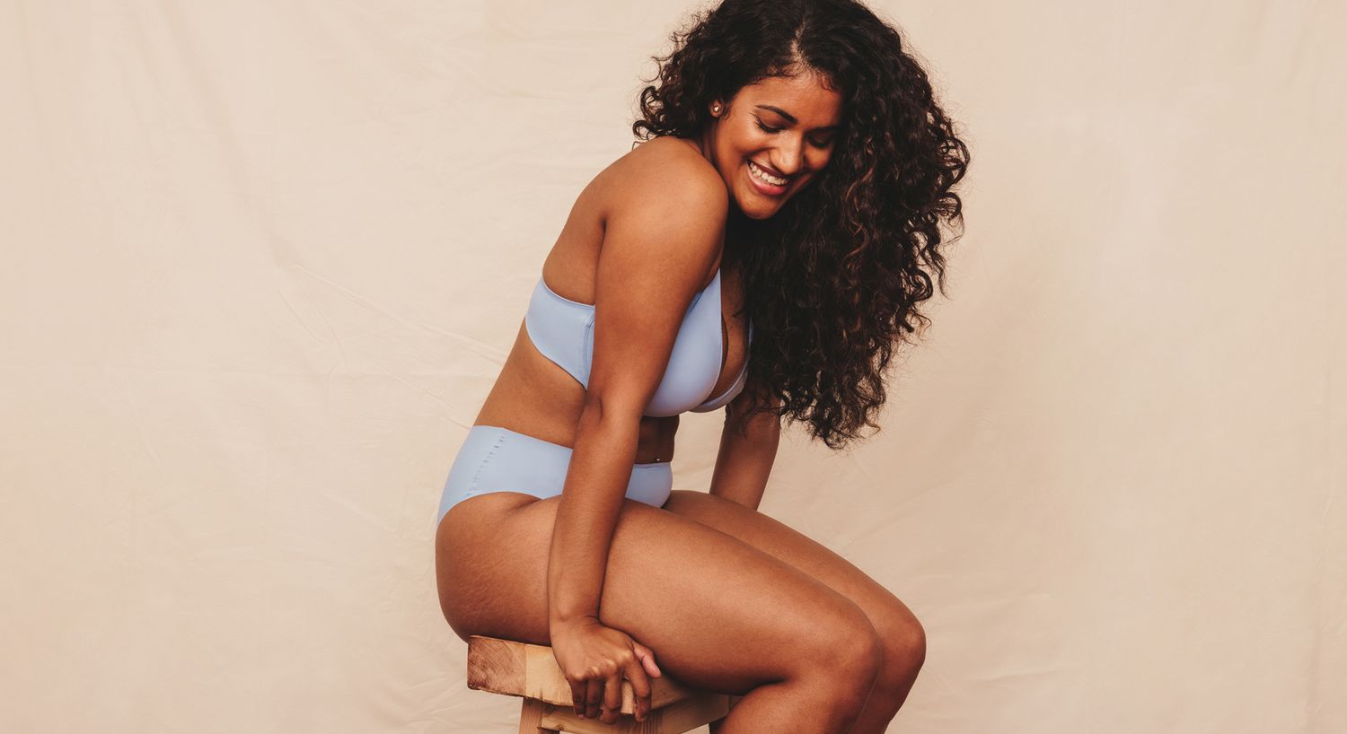 Woman in blue bikini, smiling on stool.